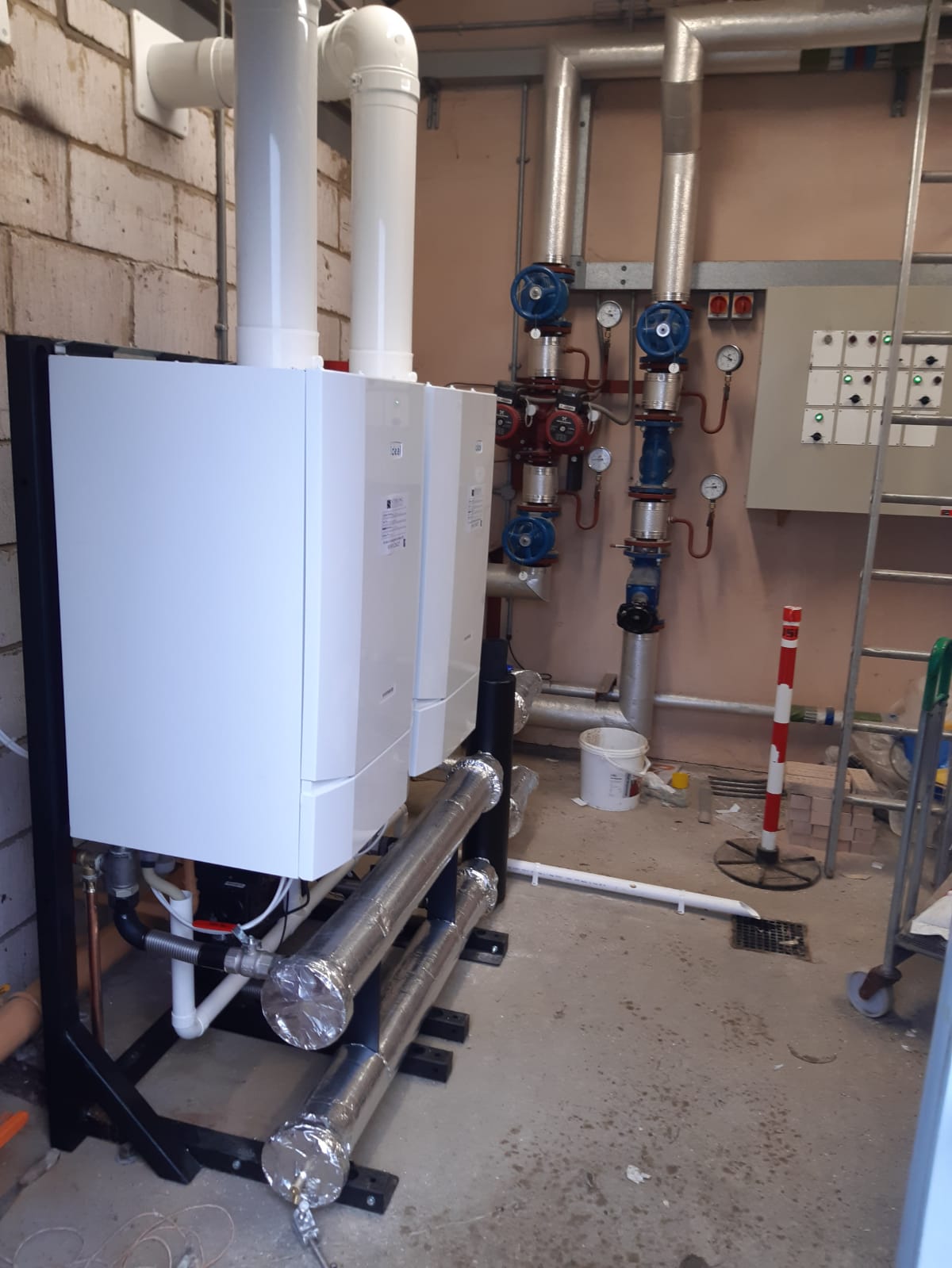 A wall-hung commercial boiler cascade on a frame with flow and return headers