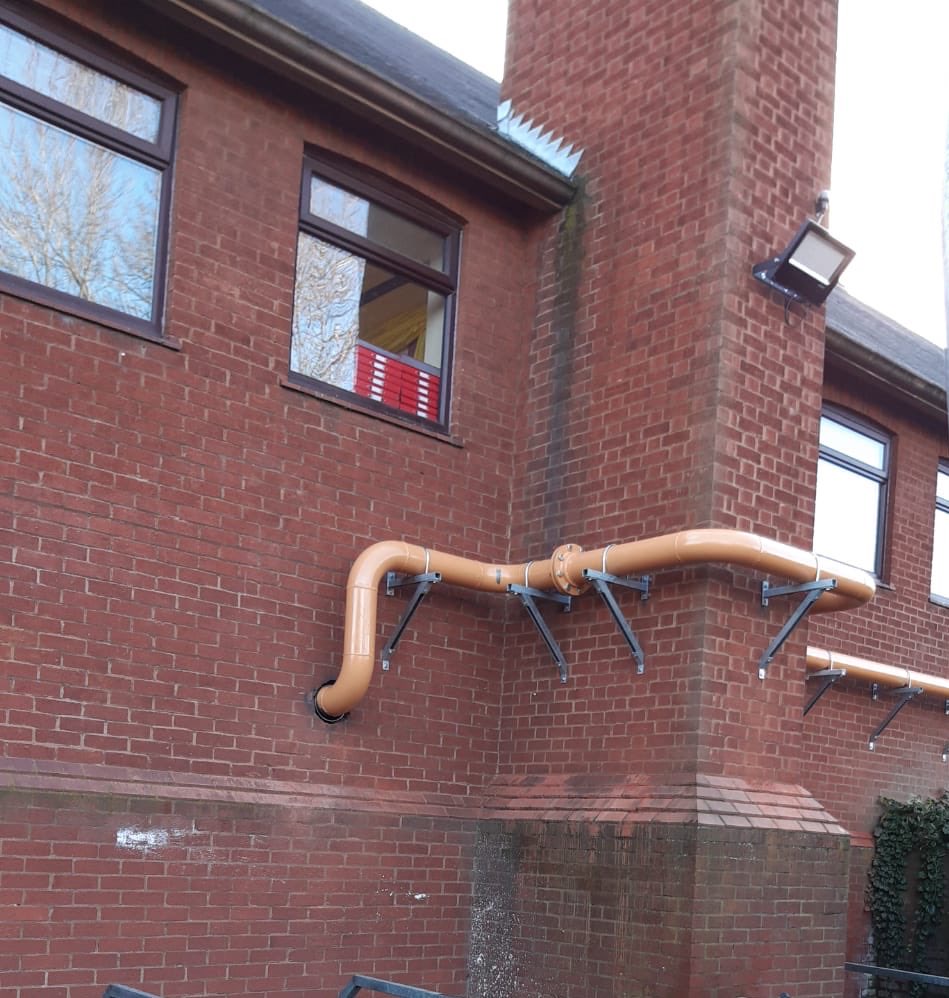 External pipework run on wall brackets along a red-brick building